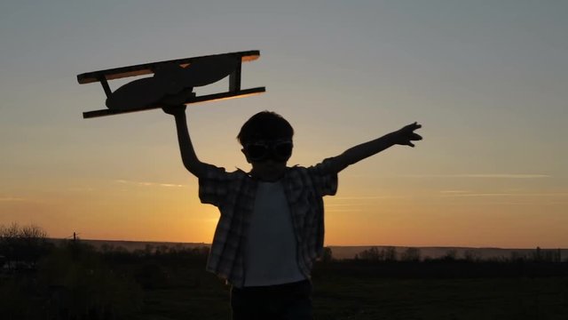 Little boy playing with cardboard toy airplane in the park at the sunset time. Concept of happy game. Child having fun outdoors.