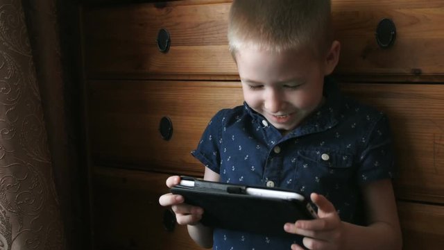 A child with a tablet, watching cartoons, smiling, slow motion
