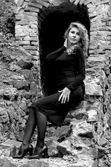 Beautiful sexy and elegant thin young light blonde european woman in total black dress and heels around old ruins in vintage style have a secret in her soul and finding the answer