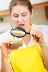 Woman inspecting potato with magnifying glass.