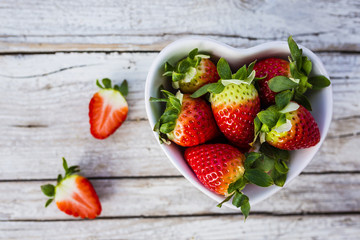 Fresh ripe strawberries in a heart shaped bowl on a wooden background.