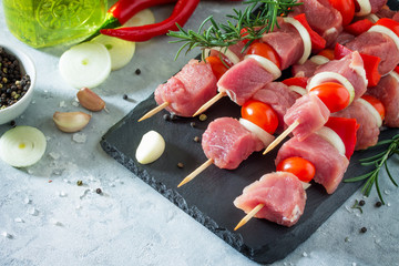 Fresh meat kebab. Meat fillet raw with cherry tomatoes, onions, spices and rosemary on a cutting board, preparation of barbecue. Copy space.