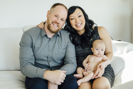 Portrait of smiling parents posing with baby daughter on sofa