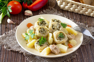 Potatoes stewed with meat and rolls of dough with garlic and greens in a plate on the kitchen table. Noodle is a national dish of Ukrainian cuisine.