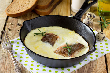 Omelette with red fish in a cast-iron frying pan on a wooden table. The concept of a healthy diet and diet.