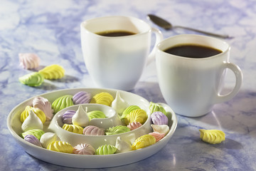 Meringue cake on a white plate and two cups of coffee on a blue marble table.