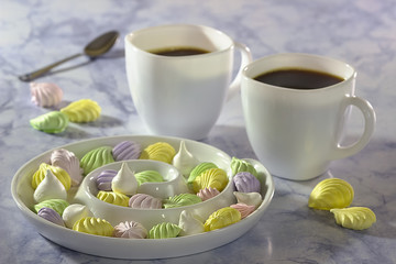 Meringue cake on a white plate and two cups of coffee on a blue marble table.