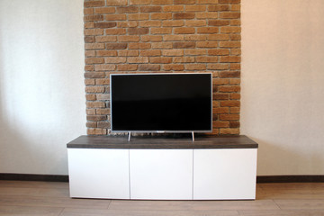 Bedside table under the TV against a brick wall
