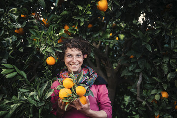 Smiling woman holding oranges under orange tree