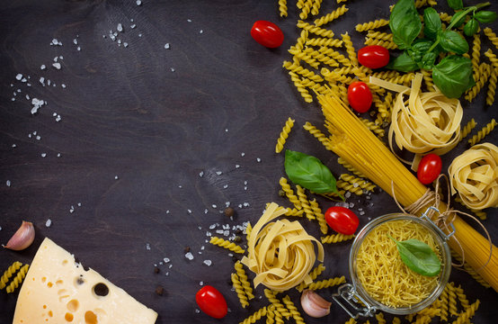 Ingredients for cooking Italian pasta - spaghetti, fusilli, fettuccine, basil, cherry tomato, garlic, pepper and cheese. Top view with space for text.