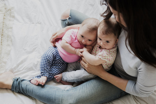 Caucasian mother sitting on bed holding twin baby daughters