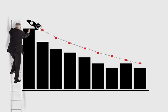 Businessman on ladder drawing graph and rocket on wall