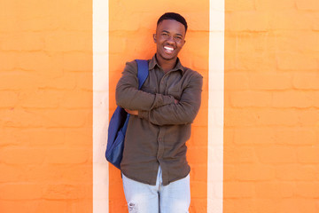 Obraz premium happy african male student standing against orange wall with bag
