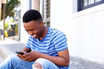 young african man sitting outside and looking at cellphone