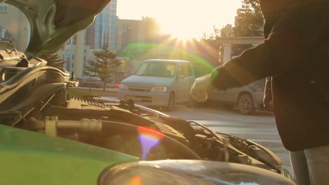 Man closes a hood of green car at the sunny city street close up