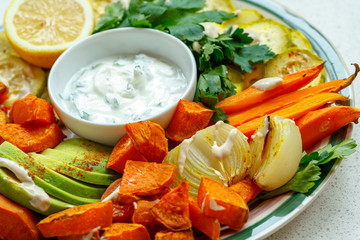 Baked sweet potato, zucchini and carrots with sour cream sauce on a plate.