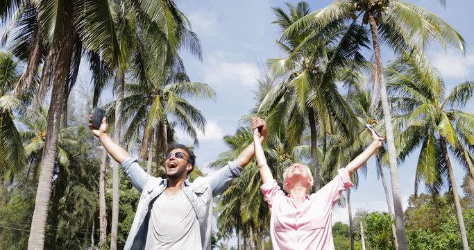 Couple Walk Using Cell Smart Phone Under Palm Trees, Man Hold Hand Up Video Call, Smiling Man And Woman Online Communication Slow Motion 60