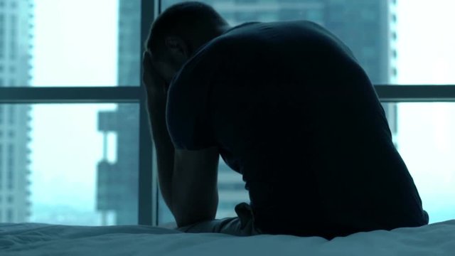 Silhouette of sad, unhappy man admire view sitting on bed at home
