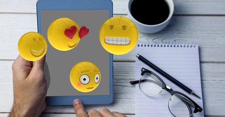 Close-up of hands using tablet PC while emojis flying over table