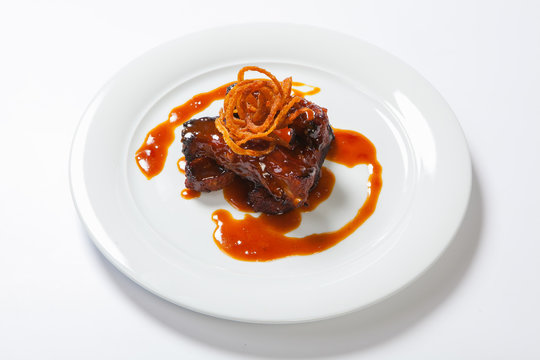 Juicy piece of lamb under red sweet sauce and covered with fried onion on large round white plate on white background.