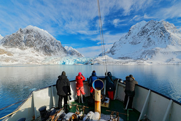 Holiday travel in Arctic, Svalbard, Norway. People on the boat. Winter mountain with snow, blue...