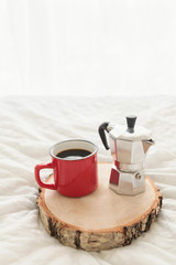 Fototapeta na wymiar Red metal cup of coffee with steel coffee maker on bed served on wooden serving board