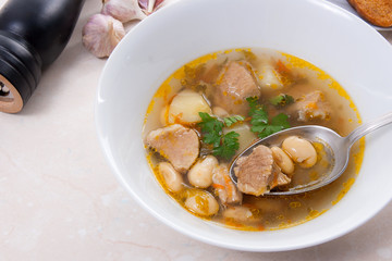 Bean soup in white plate with metal spoon, several toast on white plate on a light stone background.