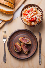 Baked potatoes with slices of bacon and eating utensils on wooden background. Sauerkraut in clay bowl and slices of white bread on cutting board..