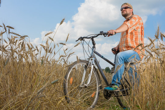 Man in cap and sunglasses standing with bicycle at the field