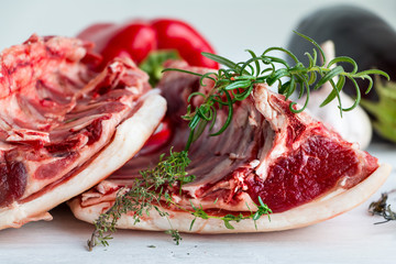 Raw red fresh saddle of mutton with herbs and vegetables on white. Closeup.