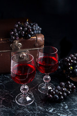 Glass of red wine on dark marble background. Cluster of blue grapes on on back background..