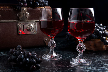 Glass of red wine on dark marble background. Cluster of blue grapes on on back background..