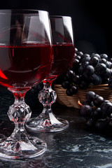Glass of red wine on dark marble background. Cluster of blue grapes on on back background..