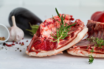 Saddle of mutton - raw red meat - with vegetables. herbs and spices on wooden table. Closeup.