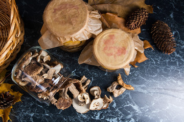 Two glass jars with wild mushrooms on black marble background.