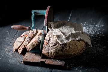 Rustic loaf of bread on slicer with on dark table