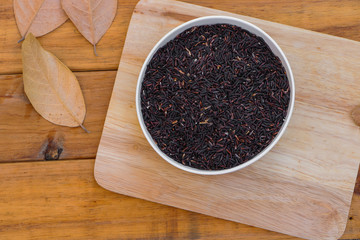 Top view of rice berry in white bowl on wood background with dry leaf.
