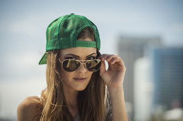Caucasian woman wearing baseball cap peering over sunglasses