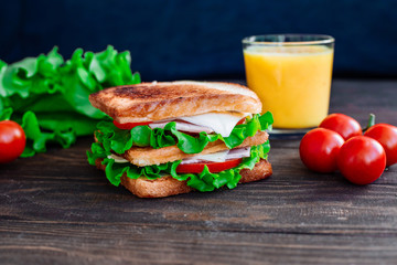 Breakfast sandwich and orange juice, tomatoes on the wooden table top view