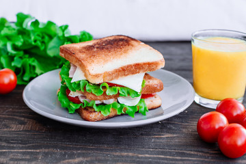 Breakfast sandwich and orange juice, tomatoes on the wooden table top view