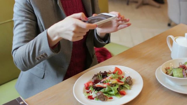 Hands of woman blogger taking photo of delicious salad with cellphone in cafe