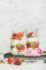 Healthy spring breakfast. Greek yogurt, granola, fresh strawberry breakfast in jars, pink raninkulus flowers, marble background, selective focus, copy space. Clean eating, vegetarian food concept