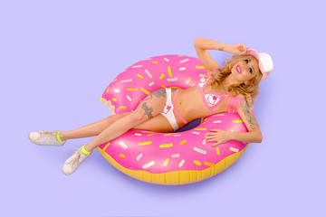 Beautiful sexy tattooed girl in studio isolated with the inflatable big donut. Dressed in a swimsuit with embroidered cakes