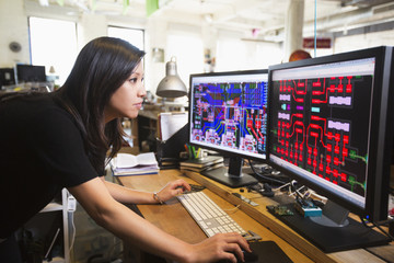 Mixed Race woman examining circuits on computer monitors