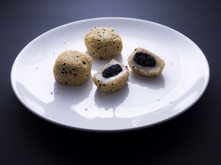 Japanese sesame mochi (sticky rice cakes) on white plate isolated on dark background