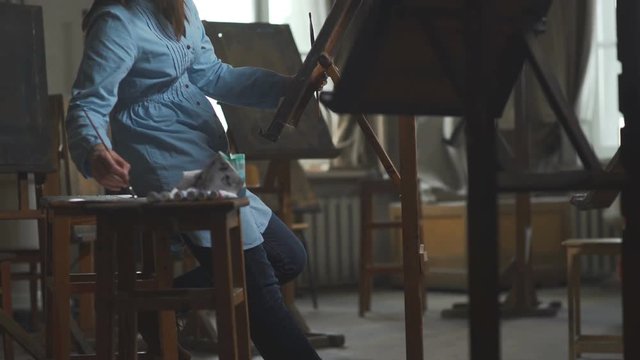 Loft-studio for the artist: a female artist paints a painting on canvas. A woman artist paints in seclusion in an atmospheric and light workshop. Artist's workshop with creative objects