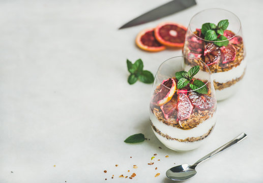 Healthy breakfast. Greek yogurt, granola and blood orange layered parfait in glasses with mint leaves over light grey marble background, copy space. Clean eating, weight loss, dieting food concept