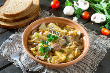 Sauerkraut with mushrooms, meat and tomato sauce with fresh vegetables on a wooden table.