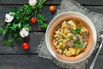 Sauerkraut with mushrooms, meat and tomato sauce with fresh vegetables on a wooden table.