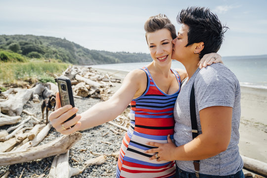 Pregnant lesbian couple posing for cell phone selfie on beach